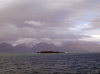 Kerguelen island: south coast - a flat rock island lies silhouetted in front of snowy mountains (photo by Francis Lynch)