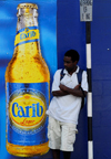 Scarborough, Tobago: man waiting for a bus in front of a drink advertising - Carib lager - photo by E.Petitalot